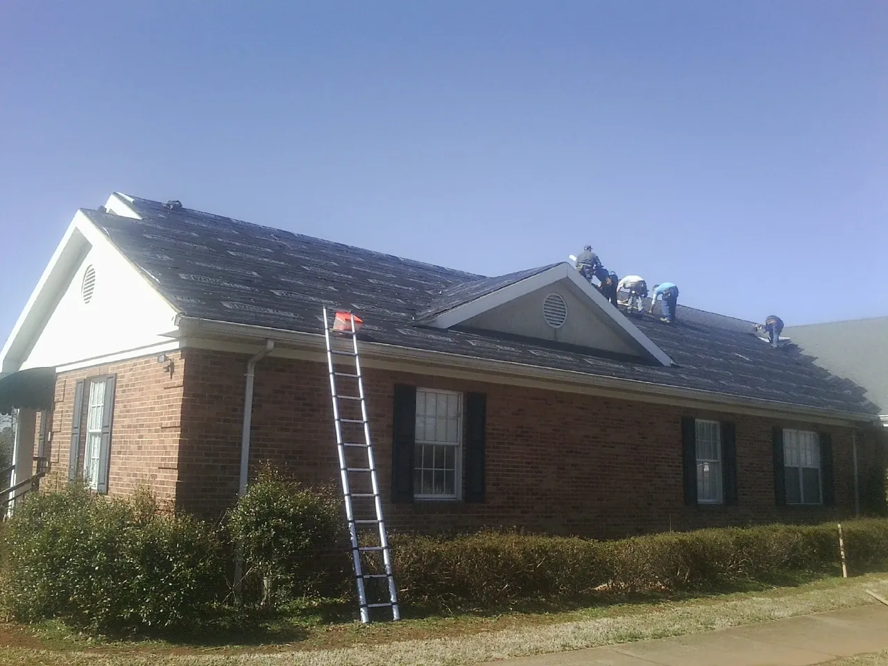 Crew tearing shingles off a brick ranch roof with a ladder set — Emergency Roof Repair work by our crew in Worthington